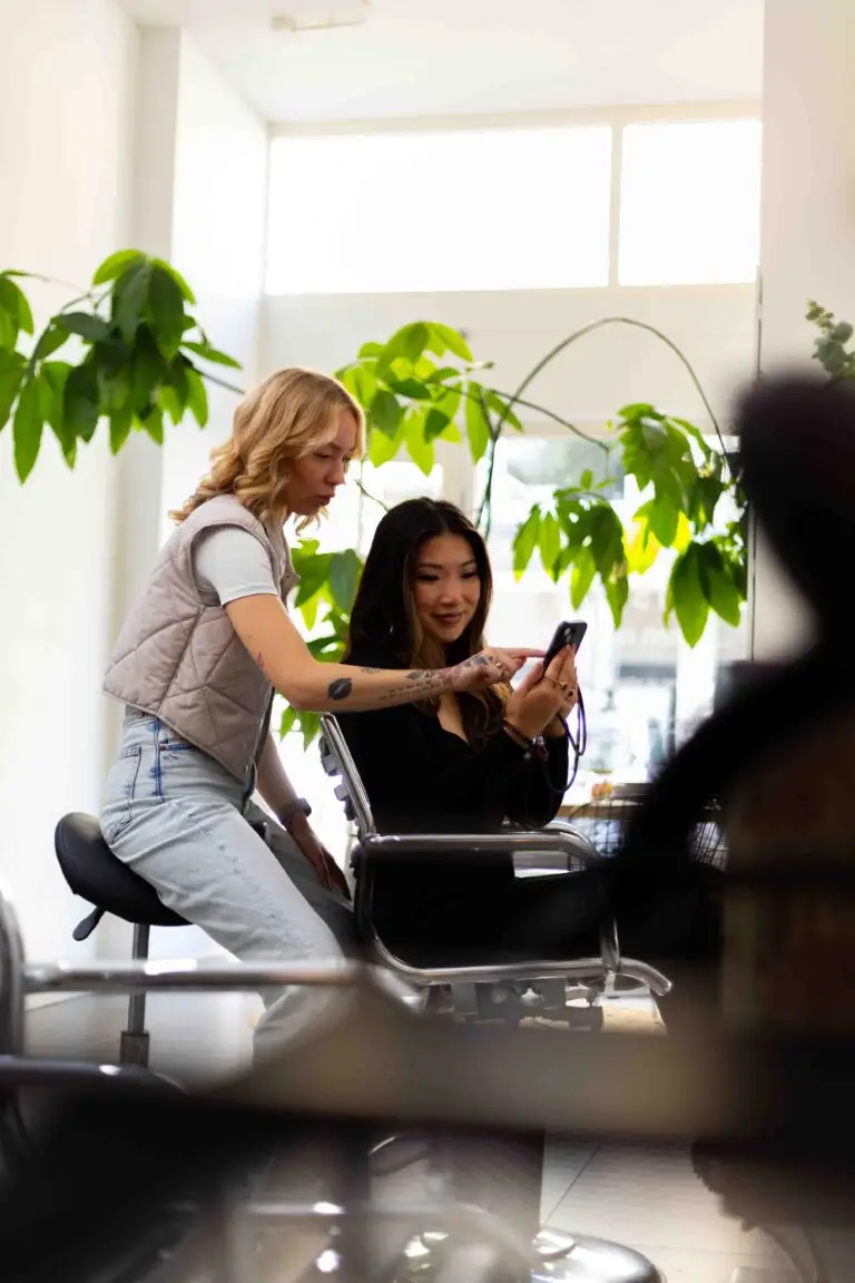 Kapster Maaike Roelofs adviseert een klant in een lichte, moderne kapsalon met groene planten op de achtergrond.