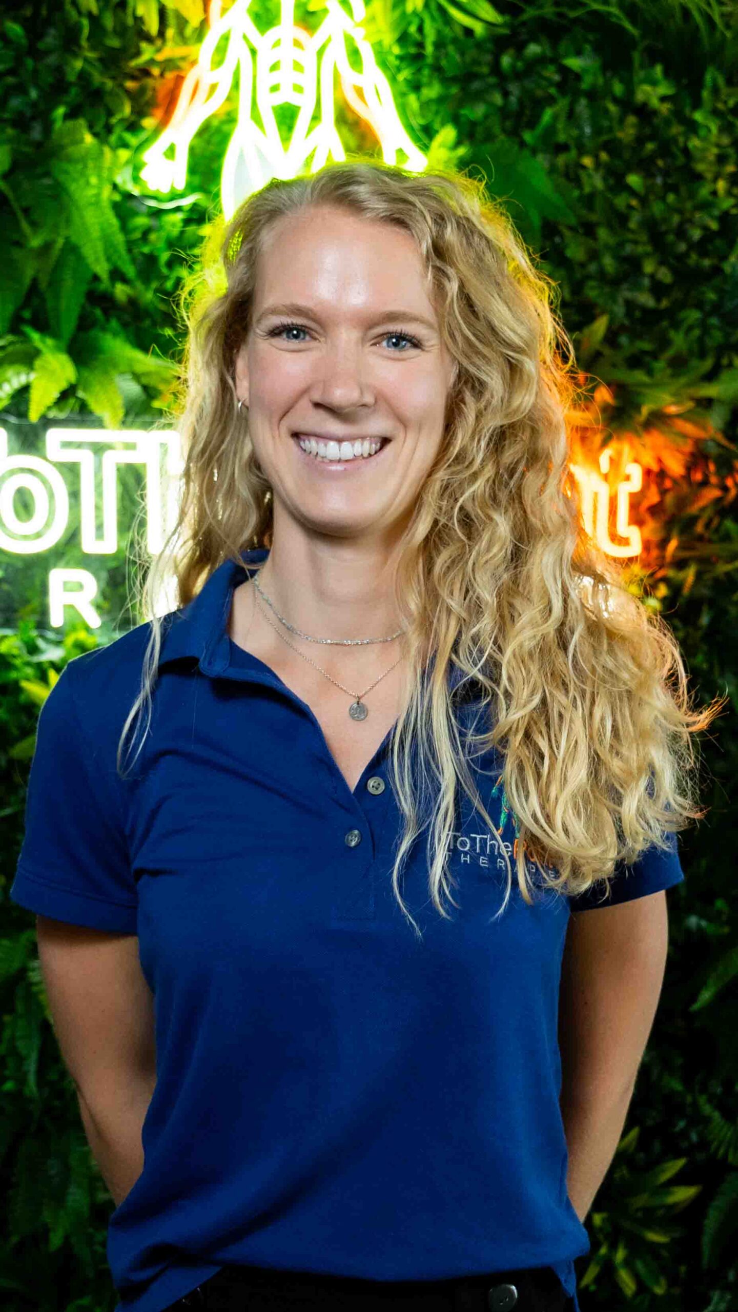 Osteopaat Iris van ToThePoint Therapie glimlacht voor de groene wand met neonlogo.