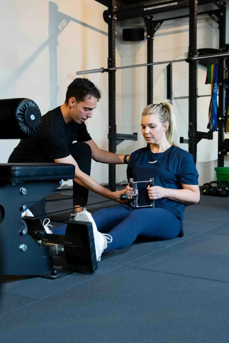 Personal trainer begeleidt een vrouw bij een seated row oefening in een professionele gymomgeving.